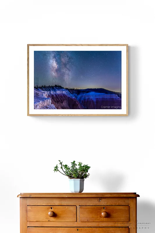 Photo of Audrey Cramer Photography's "Cedar Breaks Milky Way" on a white wall with a wooden chest of drawers and a potted plant