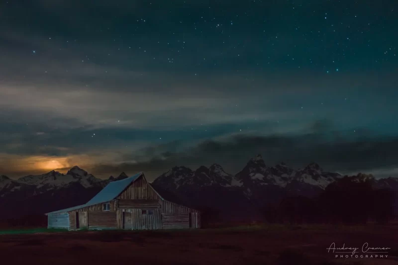 Audrey Cramer Photography's fine art landscape photograph of a light-painted Moulton barn under a setting moon and stars at Grand Teton National Park, Wyoming